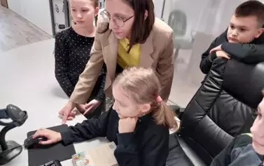 Dziewczynka pod kierunkiem bibliotekarki wprowadza dane do komputera