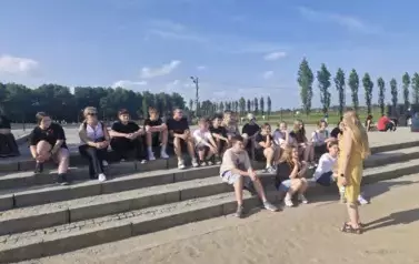 Uczniowie słuchający przewodniczki na terenie Birkenau