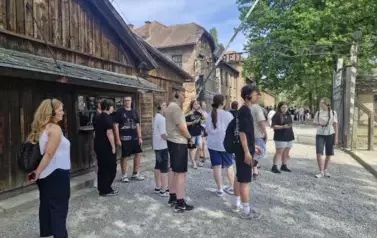 Grupa uczni&oacute;w przed bramą z napisem Arbeit macht frei