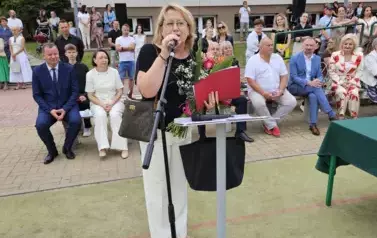 Nauczycielka odchodząca na emeryturę przemawia, z tyłu na ławkach dyrekcja i zaproszeni goście