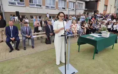 Wicedyrektor szkoły przemawia, z tyłu na ławkach dyrekcja i zaproszeni goście