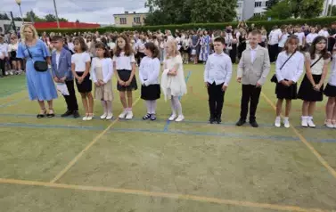Grupa wyr&oacute;żnionych uczni&oacute;w klasy trzeciej z wychowawcą stoją na środku