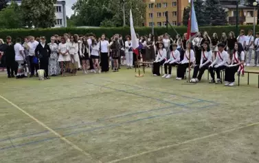 Grupa uczni&oacute;w klas starszych stoi, na ławkach siedzą członkowie poczt&oacute;w