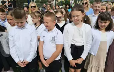 Grupa uczni&oacute;w klas młodszych z wychowawczynią, za nimi rodzice