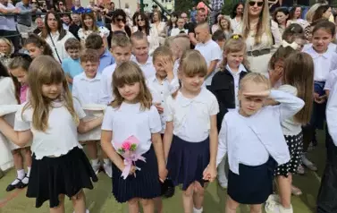 Grupa uczni&oacute;w klas młodszych, za nimi rodzice