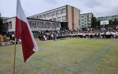 Szeroki widok na boisko i wszystkich uczestnik&oacute;w, na pierwszym planie flaga biało-czerwona