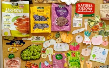 Tablica, na kt&oacute;rej prezentowane są opakowania zdrowych przekąsek oraz owoce i warzywa