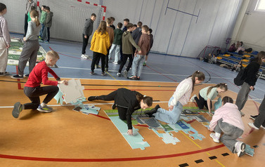 Uczniowie na hali sportowej układają puzzle dużego formatu