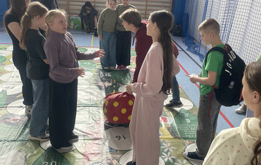 Uczniowie grają dużą miękką kostką na macie przyrodniczej pod czujnym okiem Pań ze ZGOKu Rzęd&oacute;w