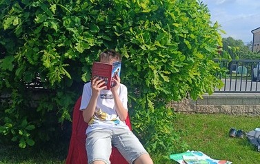 Uczeń klasy 4B na czerwonym krześle czyta lekturę
