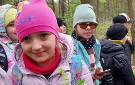 Dziewczynka w r&oacute;żowej czapce prezentuje leśną roślinę