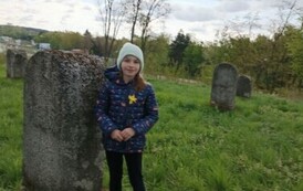 Dziewczynka w granatowej kurtce przy macewie