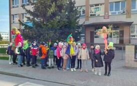 Grupa dzieci z kukłami marzanny przed budynkiem szkoły