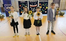 Czworo uczni&oacute;w z kwiatami recytuje wiersz