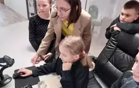 Dziewczynka pod kierunkiem bibliotekarki wprowadza dane do komputera