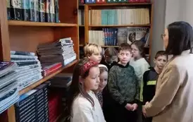 Uczniowie z bibliotekarką na tle regał&oacute;w z książkami