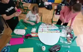 Trzy dziewczynki wyklejają guzikami pisankę