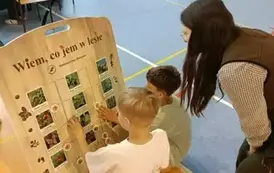 Uczniowie i pracownica Nadleśnictwa przy planszy edukacyjnej