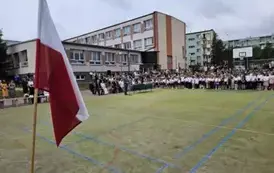 Szeroki widok na boisko i wszystkich uczestnik&oacute;w, na pierwszym planie flaga biało-czerwona