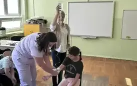 Pielęgniarka pokazuje na ręce uczennicy jak zakładany jest wenflon i kropl&oacute;wka