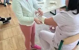 Uczniowie obserwują jak jedna z uczennic bandażuje rękę pielęgniarce