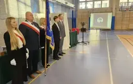 Poczet Rady Rodzic&oacute;w, przewodniczący Samorządu Uczniowskiego, wicedyrektor R. Konat podczas uroczystości. W tle na ekranie zdjęcie nowego sztandaru