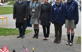 Dyrektor, nauczyciele i uczniowie składają kwiaty pod pomnikiem