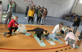 Uczniowie na hali sportowej układają puzzle dużego formatu