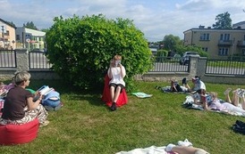 Uczniowie klasy 4B czytają fragmenty lektury placu przy szkole-w centrum uczeń na czerwonym krześle