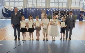 Grupa wyr&oacute;żnionych uczni&oacute;w klas trzecich z dyplomami, z lewej wicedyrektor, z prawej dyrektor szkoły