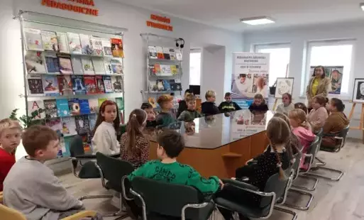 Uczniowie siedzą w bibliotece na tle ekspozycji książek
